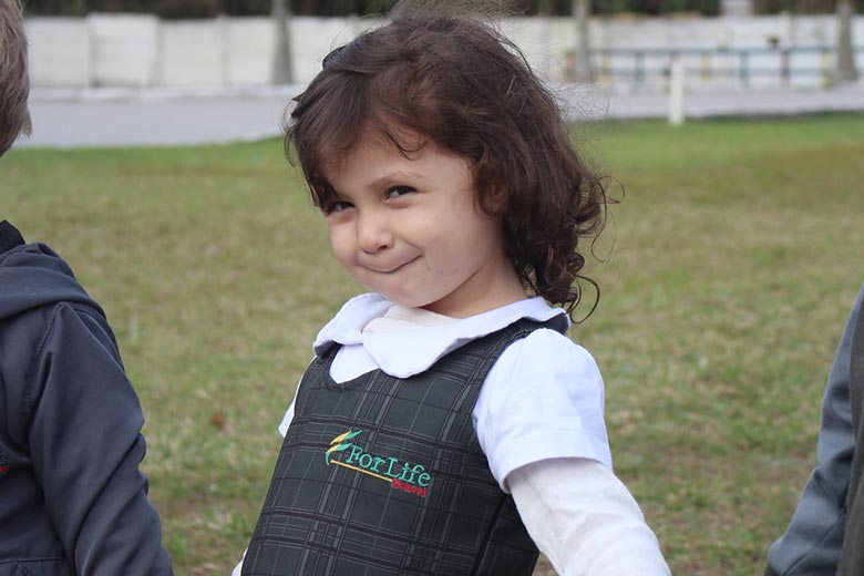 Menina sorrindo de mãos dadas com amigos em escola cristã bilíngue