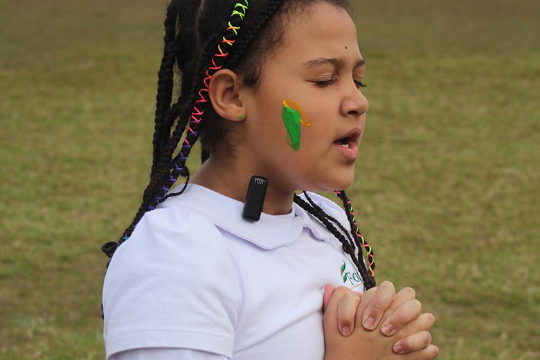 Aluna de olhos fechados fazendo uma oração ao ar livre em escola cristã bilíngue